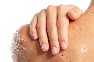 Hand exfoliating a shoulder with visible skin body scrub texture on a white background