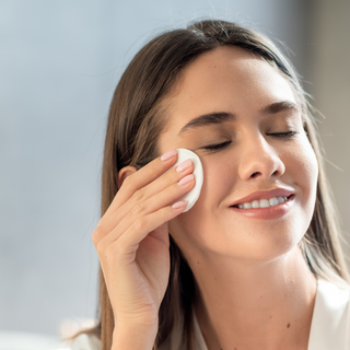 Woman applying a facial product with a cotton pad against a neutral background