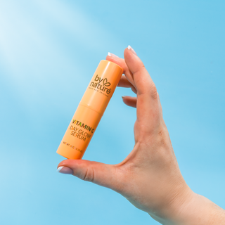 Hand holding an 'by nature' vitamin serum against a blue background